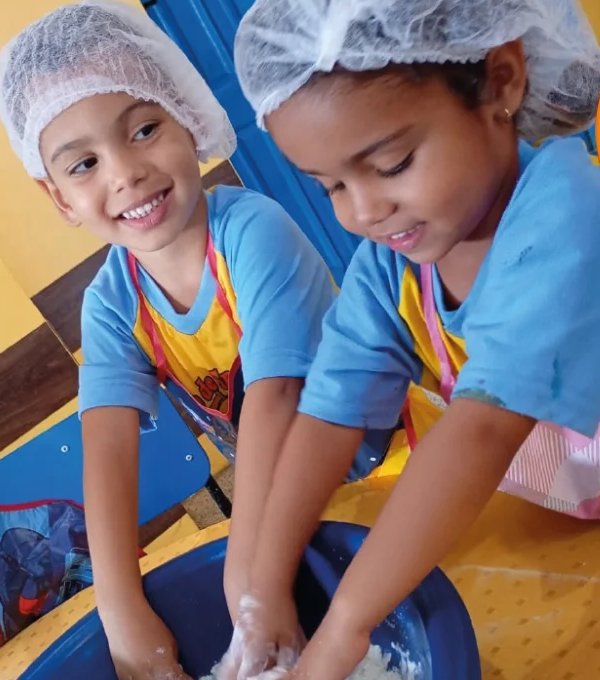 Duas alunas do Centro de Ensino Lira amassando a massa numa bacia durante atividade de culinária