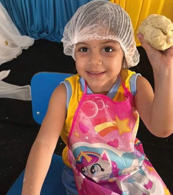 Aluna do Centro de Ensino Lira, de touca e avental, segurando a massa do pão ázimo