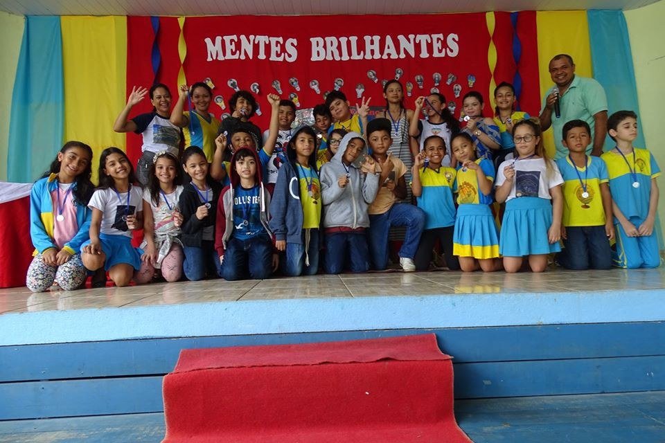 Turma do Centro de Ensino Lira reunida no palco durante o projeto Mentes Brilhantes, com uniforme azul e amarelo